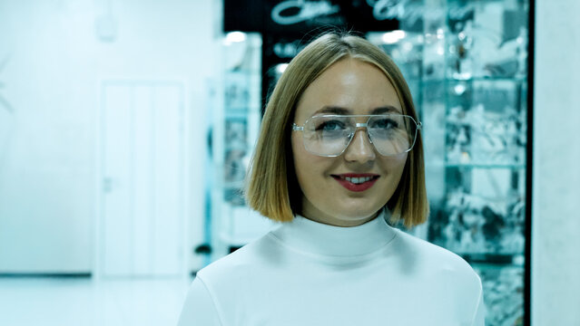 Smiling woman in glasses poses in a modern optical store setting