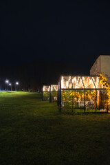 Cozy illuminated garden cabins glow warmly at night on an open lawn, creating a festive and inviting atmosphere in the dark.