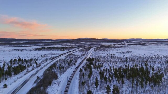 Freight train with iron ore, aerial view, Sunset over arctic mountain landscape in Lapland, Sweden, road and railroad between Kiruna and Narvik