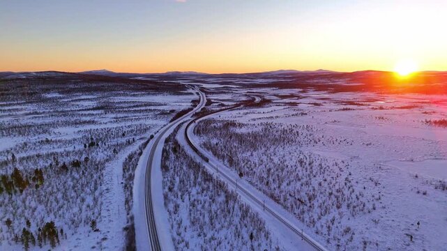 Sunset over arctic landscape in Lapland, Sweden, road and railroad between Kiruna and Narvik, with a freight train passing by