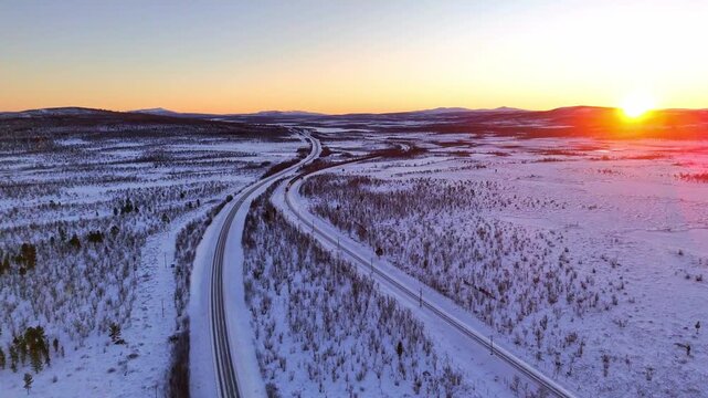 Sunset over arctic landscape in Lapland, Sweden, road and railroad between Kiruna and Narvik, with a freight train passing by