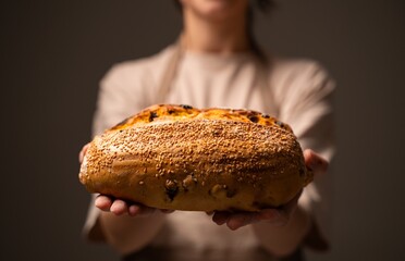 Female artisan baker holding seeded bread loaf with golden crust and rustic handmade texture in warm lighting