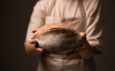 Female artisan baker presenting rustic round bread loaf with cracked crust in warm soft studio lighting