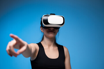 Woman wearing VR headset pointing forward while engaging with virtual interface in digital blue studio