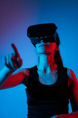 Female gamer using VR headset and pointing forward while interacting with neon virtual interface