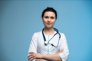 Female doctor with stethoscope posing confidently against blue background in professional uniform