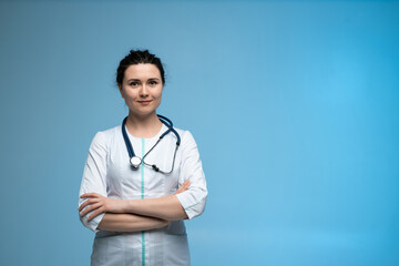 Female doctor with stethoscope standing confidently in white uniform on clean blue studio background