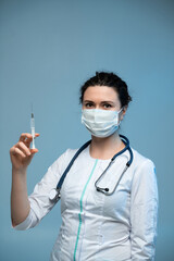 Nurse holding syringe preparing vaccination while wearing medical mask and uniform on blue background