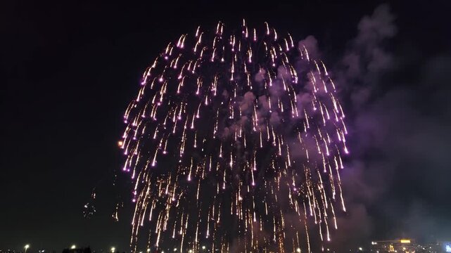 Purple Fireworks Burst in Night Sky - A dazzling burst of purple fireworks illuminates the dark night sky. Wisps of smoke linger in the air as the vibrant colors create a festive display.