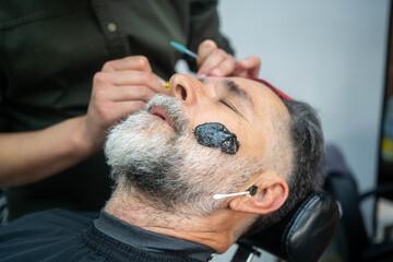 Fototapeta premium Barber grooming customer’s beard professionally in modern salon