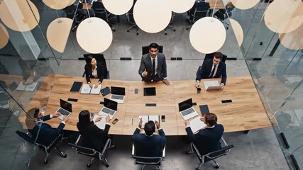 High angle view of assertive businessman leading a formal meeting with diverse team members around a large wooden conference table