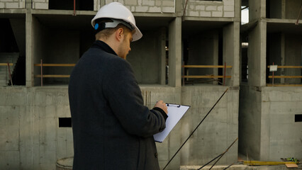 Male engineer stands and talks on his phone, looking at the incomplete structure
