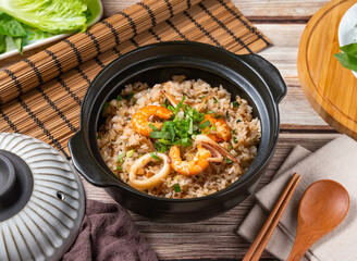 Seafood fried rice with shrimp and squid served in a black bowl. Perfect for showcasing a tasty Asian meal on a wooden table.