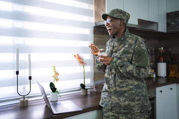 Smiling african american soldier eating breakfast and looking at laptop in kitchen