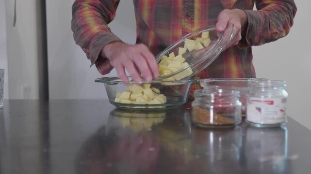 Preparing a Meal: Transferring Freshly Diced Potatoes into a Glass Bowl with Spices on the Side.