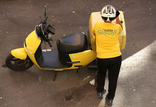 Repartidor en moto de Glovo llevando y entregando pedido