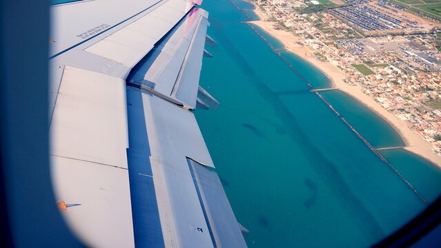 Airplane wing extending over the beautiful blue sea and a densely populated coastal town, symbolizing air travel, holidays, and exploring new tourist destinations