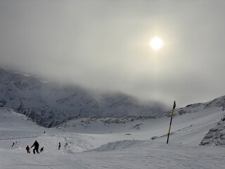 Ski slope in the Alps with gondola lift and skiers. Snowy mountains in the background under a cloudy sky, creating a typical winter scene. © Art-Park