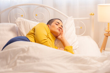 Cheerful young woman with buzz cut enjoying playful morning in cozy bedroom, covered in white blanket, expressing happiness, relaxation, and positive lifestyle in natural light.