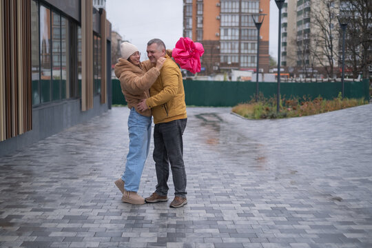 Couple shares a moment on a rainy day in an urban area while one carries a large pink gift bag - Powered by Adobe