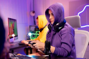 young woman in a purple hoodie working or gaming at a computer in a modern, neon-lit room, digital lifestyle, remote work, live streaming, or esports. Gamer controlling joystick for video game.