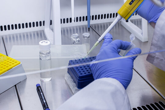 A scientist holds a small test tube containing DNA and an autosampler at his workstation in the lab. He's preparing a reagent mixture for PCR.