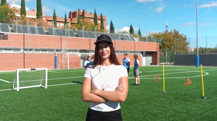 Portrait of a proud young female soccer coach with her arms crossed, smiling at the camera on a sunny day during a training session