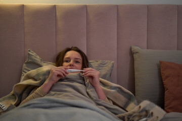 Female lying in bed checking thermometer while resting