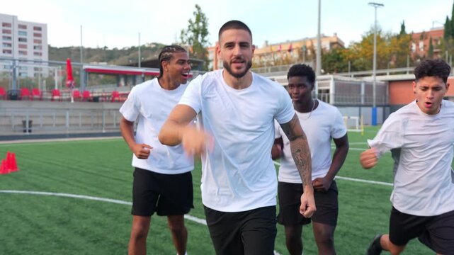 Group of determined multiethnic soccer players running towards camera, celebrating a win together and hugging in a huddle on the field