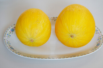 two yellow melons on a white plate in a kitchen