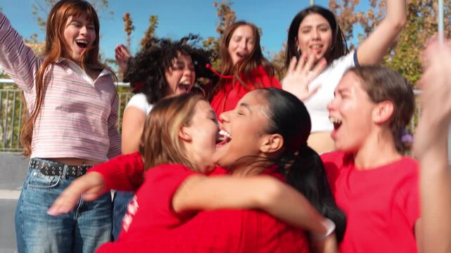 Group of excited young multiracial women in red celebrating a goal. Enthusiastic soccer fans jumping and hugging in the stadium bleachers
