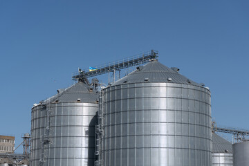 Modern industrial grain silos feature corrugated metal exteriors standing tall against a bright blue sky, showcasing agricultural storage technology.