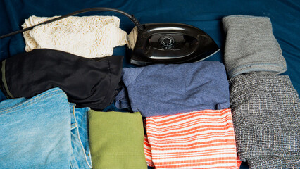 Top view of folded clothes next to an iron on a bed