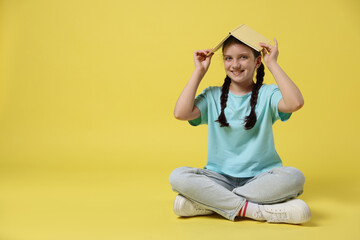 Cute girl with book on yellow background, space for text