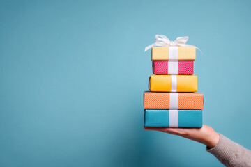 Colorful stacked gifts held by a hand against a blue wall background during a celebration or special occasion