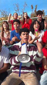 Young, excited crowd of supporters cheering for their favorite team at a live sports event. Cheerful friends enjoying the match and celebrating victory