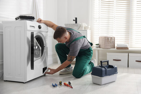Repairman examining broken washing machine at home
