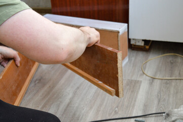 a person holding a wooden kitchen drawer removed from a cabinet during a renovation. the inside of the drawer is freshly painted white, while the exterior remains in its original brown finish.