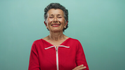 Senior woman smiling with grey hair wearing red shirt standing against blue background showcasing joyful expression and positive attitude.