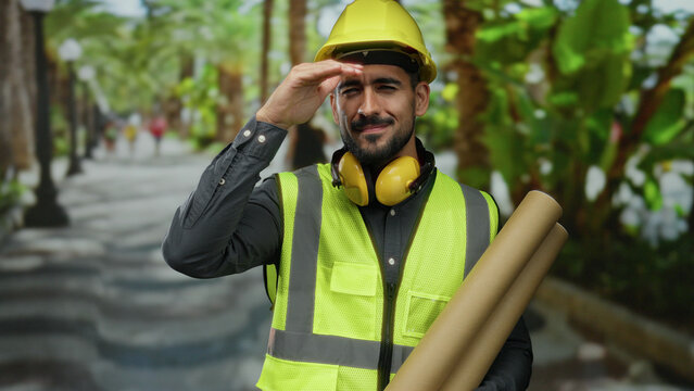 Man wearing construction helmet and high-visibility vest holding blueprints while looking into distance on a sunny urban street with palm trees. - Powered by Adobe