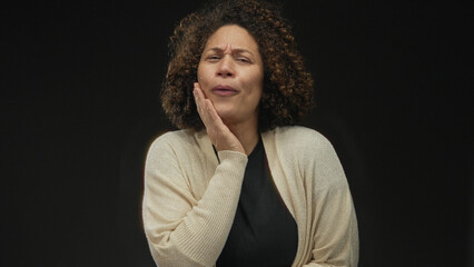 Woman places both hands on chest in a grateful gesture in studio with black background, view of hands and face showing a thankful expression; gratitude warmth compassion.