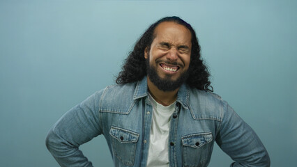 Fototapeta premium Man wearing denim jacket with hands on hips looking down in a pale blue studio; frustration fatigue.