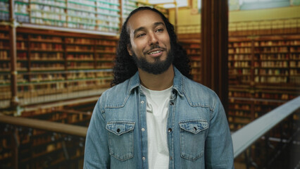 Man with beard smiling and looking sideways in a library building among bookshelves and railing  thoughtful curiosity. © Krakenimages.com