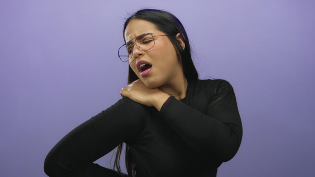 Woman in glasses massaging her shoulder in discomfort, isolated against a purple background, expressing pain relief needs. - Powered by Adobe
