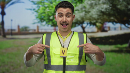 Young hispanic man wearing reflective vest as volunteer in outdoor park setting showcasing community service involvement