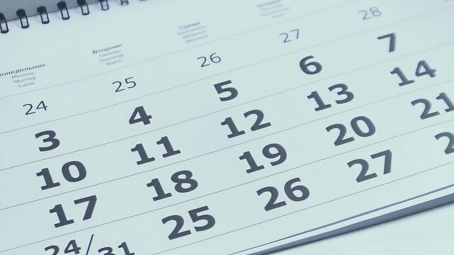 Close up of a white paper calendar as pages rapidly turn upward, dates and months flying by to symbolize the fleeting passage of time, busy schedules and approaching deadlines