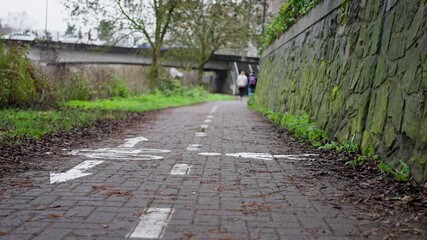 leisurely hike through tranquil garden surroundings, peaceful riverside walk among historic bricks and lush greenery, unhurried trek along damp pathway beside calm waters and ancient stone structures