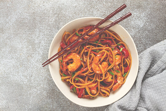 udon stir-fry shrimp noodles with red bell pepper and green onion, served in a black bowl, with chopsticks, gray background, - Powered by Adobe
