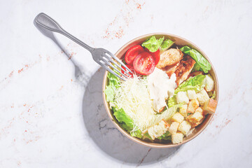 Caesar salad, in a disposable paper container, with a fork on the table, hard light,