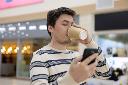 A young man with a cup of sobo coffee and a phone in a shopping mall or office. Concept of the fast pace of city life.